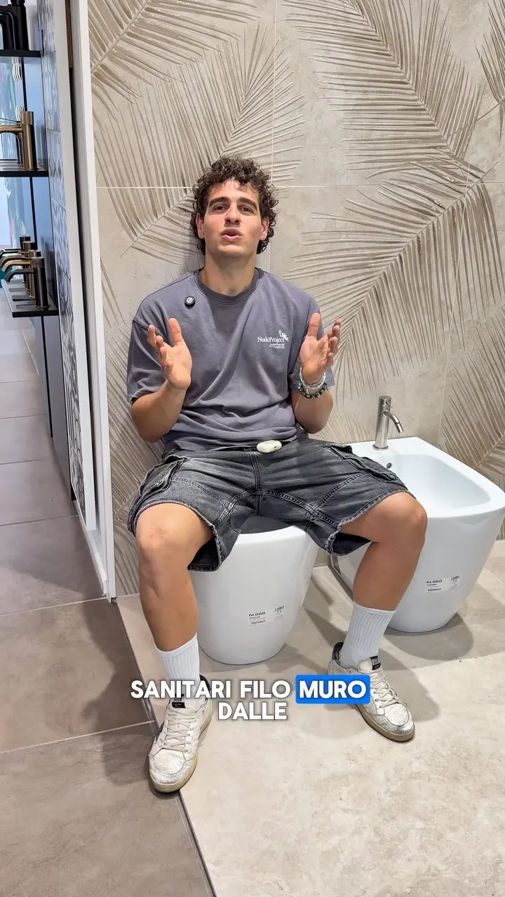 Un ragazzo seduto su un vaso filo muro nello showroom mentre spiega le misure, accanto al bidet abbinato